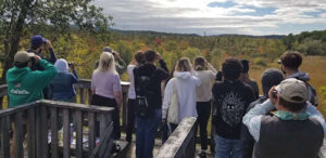 Students stand on a platform using binoculars. The 2022 Environmental Studies Class examines a bald eagle at the Ramshorn-Livingston Audubon Sanctuary in Catskill.