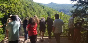 The 2022 River Ecology Class at the Kaaterskill Falls Overlook. Students learn about the history of the region, including the Hudson River School of Art and the great mountain houses. Students gathered on a platform overlooking Kaaterskill Falls. 