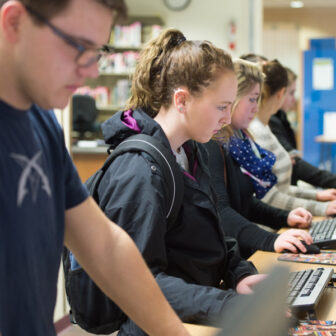Students standing and working on row of computers