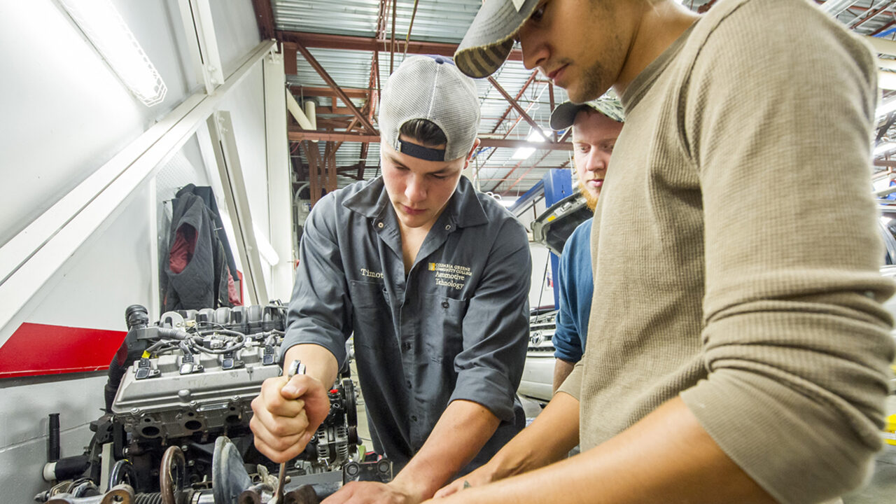 Two, white male students working on a car engine in the automotive technology lab