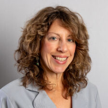 woman with curly, shoulder-length, brown hair with gray blazer smiling in a headshot