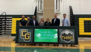 Seven individuals standing behind a sign that reads "Thank you Bank of Greene County," in the gymnasium.