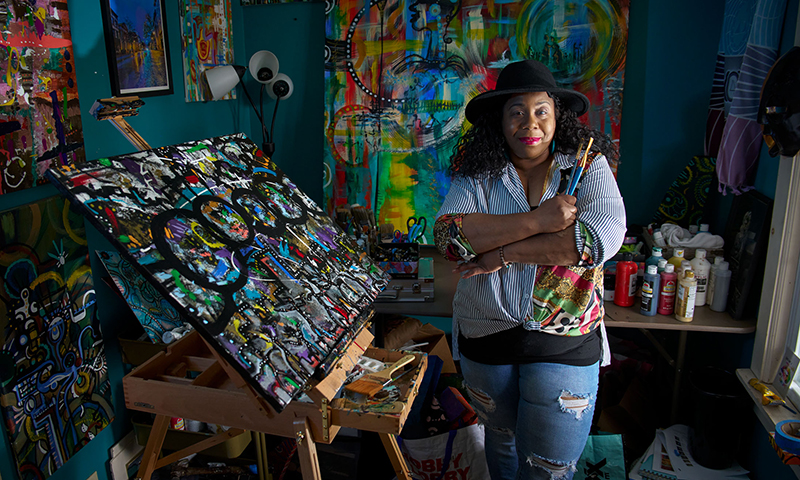 African American female artist standing next to an easel in a colorful art studio
