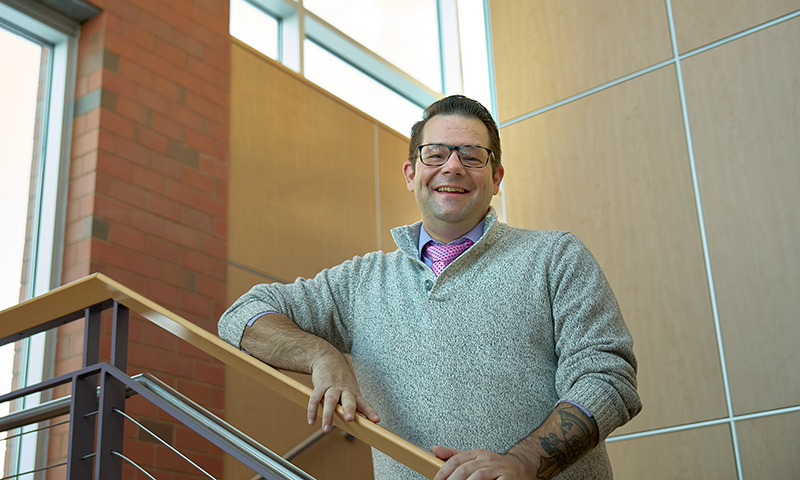 Caucasian male standing at the top of a stairwell smiling