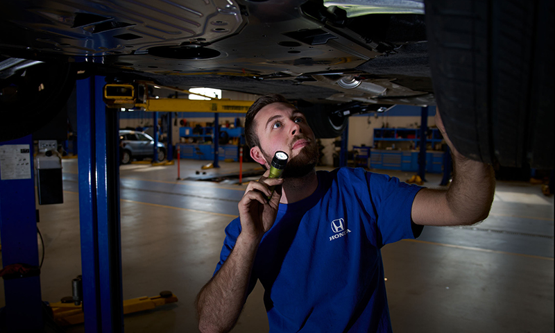 Caucasian male in blue shirt with flashlight in an automotive shop.