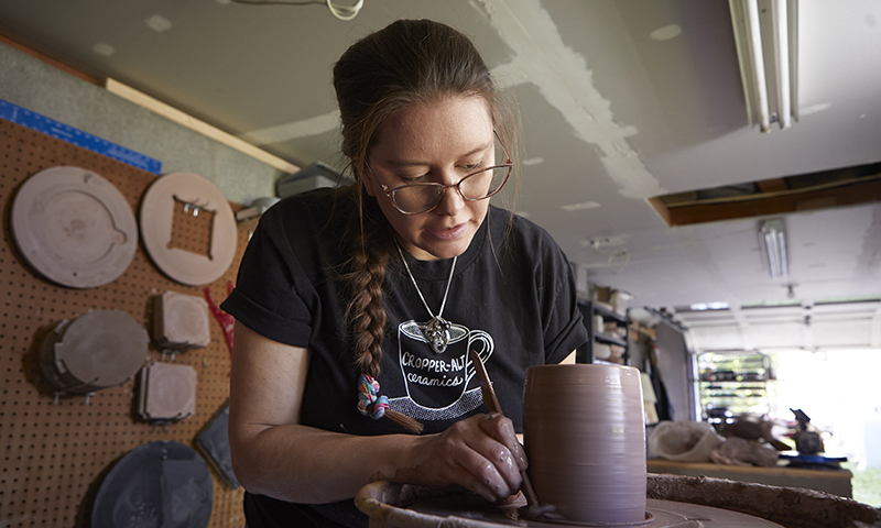 Caucasian women hunched over working on a ceramic vase in ceramic studio