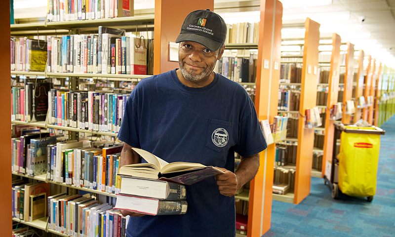 African American male wearing a baseball hat thumbing through books in library