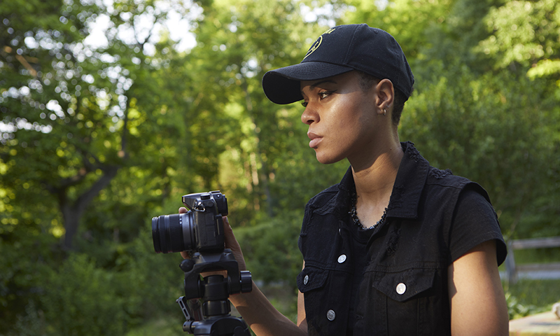 African American female outdoors standing behind a camera on a tripod