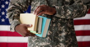 Man in fatigues holding books in front of an American flag